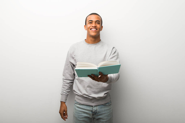 Afrikanisch-amerikanischer Mann auf weißem Wandhintergrund hält ein Buch und gibt es jemandem - Foto, Bild