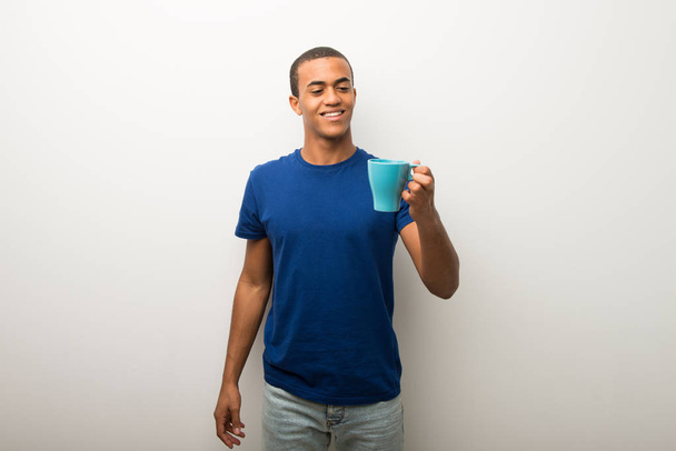 Mladý Američan Afričana muž na bílé zdi držící šálek horké kávy - Fotografie, Obrázek