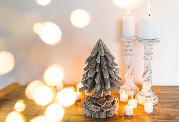 White wooden Decorated Christmas Tree with Candles and Golden blurred shiny lights around. Place for Text. Hand Made Festive Concept - 写真・画像