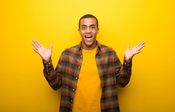 Afro-amerikai fiatalember élénk sárga háttérrel, a meglepetés, és a döbbent arckifejezés - Fotó, kép