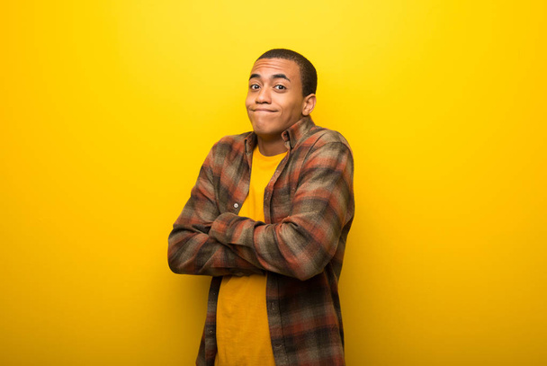 Young african american man on vibrant yellow background making doubts gesture while lifting the shoulders - Foto, afbeelding