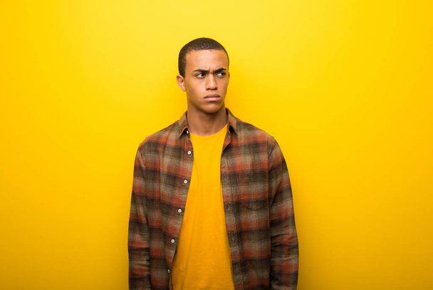 Young african american man on vibrant yellow background feeling upset - 写真・画像
