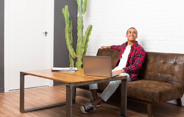 Afrikai amerikai férfi a nappaliban jelentő karral, csípő, és nevetve laptop - Fotó, kép
