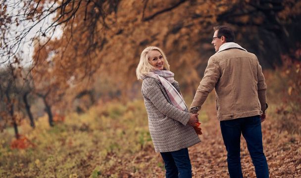 Senior couple walking in park in autumn. Attractive woman and handsome man spending time together outdoors - Foto, immagini