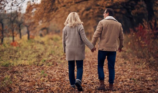 Senior couple walking in park in autumn. Attractive woman and handsome man spending time together outdoors - Φωτογραφία, εικόνα