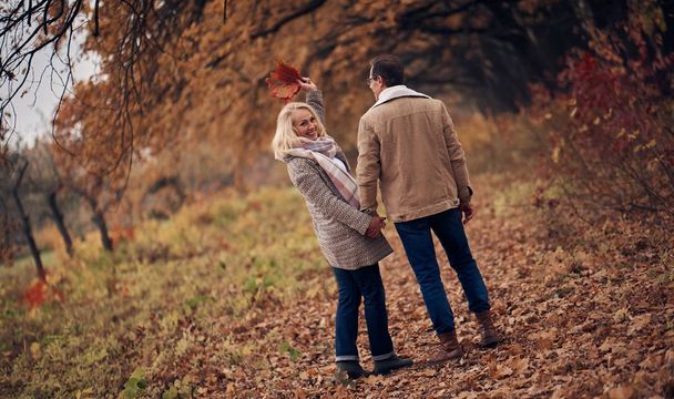 Senior couple walking in park in autumn. Attractive woman and handsome man spending time together outdoors - Foto, Imagen