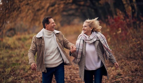 Senior couple walking in park in autumn. Attractive woman and handsome man spending time together outdoors - Zdjęcie, obraz