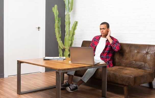 Afrikai amerikai férfi a nappaliban, hallgat valami azáltal, hogy kezét a fül laptop - Fotó, kép