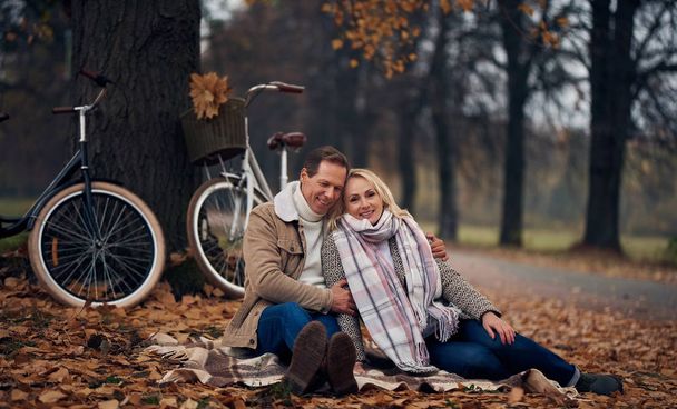Senior couple walking in park in autumn. Attractive woman and handsome man spending time together with bicycles - Фото, изображение