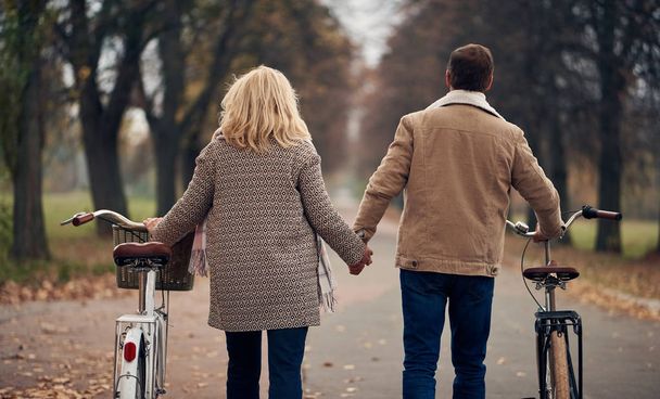 Senior couple walking in park in autumn. Attractive woman and handsome man spending time together with bicycles - Foto, Imagem