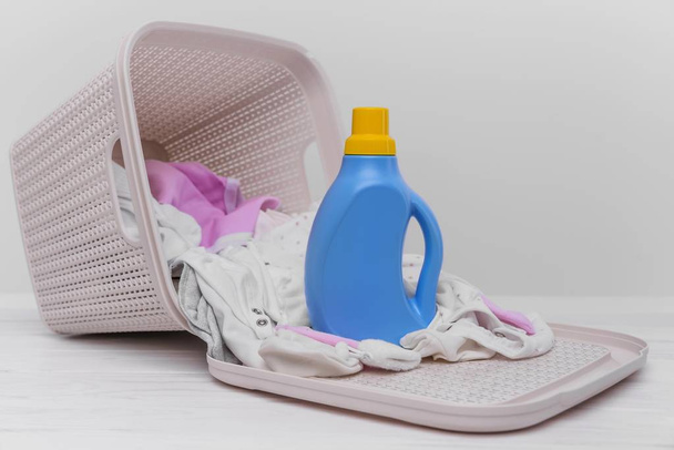 Bottle of laundry detergent in the basket with dirty baby clothes. - Photo, Image