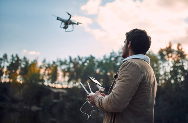 Male tourist exploring new places. Handsome bearded man on nature with quadcopter. Using drone while standing near lake. - Fotoğraf, Görsel