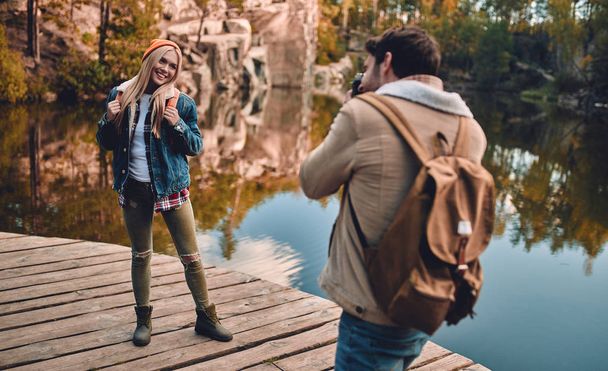 Young couple of tourists are exploring new places. Attractive young woman and handsome bearded man are spending time together on nature and making photo on a retro camera. - Fotografie, Obrázek