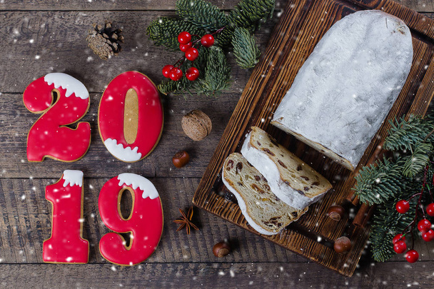 Stollen Χριστούγεννα σε ξύλινα φόντο με αριθμό cookies 2019. Παραδοσιακό χριστουγεννιάτικο επιδόρπιο ζαχαροπλαστικής με προβολή επάνω εορταστική διακόσμηση, επίπεδη θέσει - Φωτογραφία, εικόνα