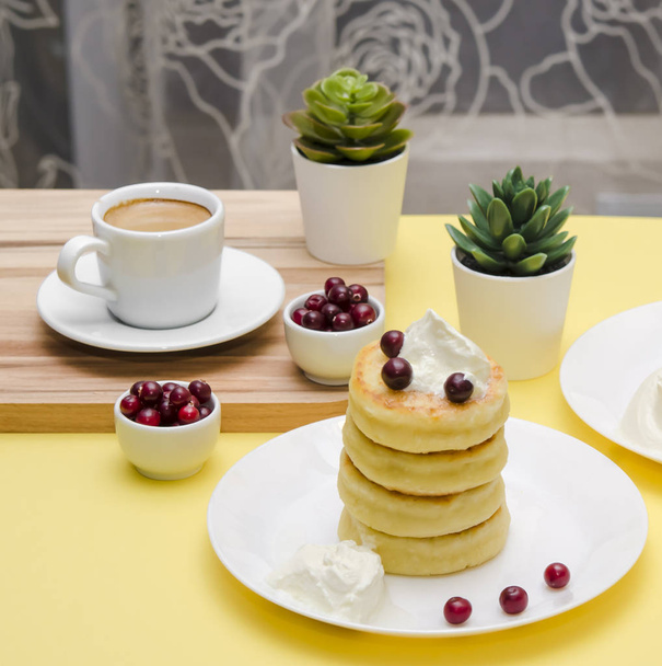 Quark-Pfannkuchen mit saurer Sahne und Beeren auf gelbem Hintergrund. syrniki. Russisches Essen. Kopierraum. - Foto, Bild