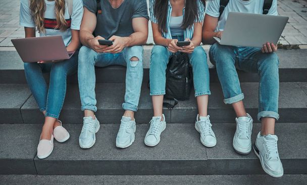 Group of young people are studying together in university. Cropped image of students outdoors sitting on stairs. - Foto, Imagem