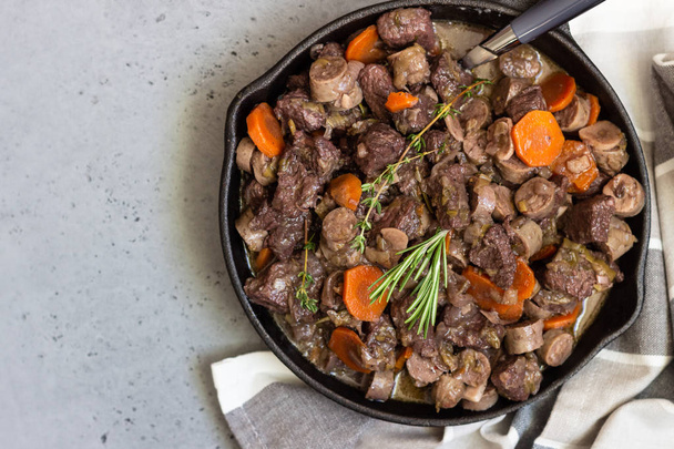 A skillet with beef bourguignon or meat stewed with sausages, carrots, garlic, onion, red wine, fresh herbs and spices. - Zdjęcie, obraz