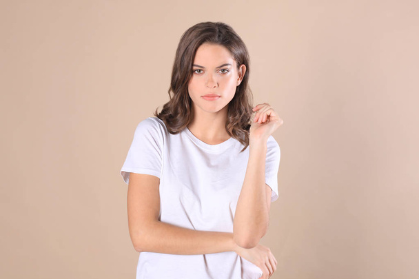 Cheerful brunette woman dressed in basic clothing looking at camera, isolated on beige background. - 写真・画像