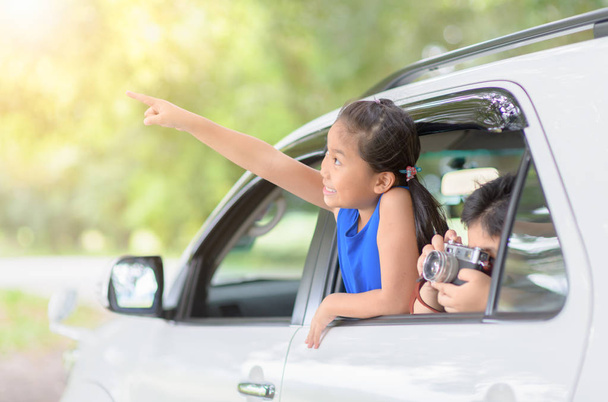 Ευτυχισμένος κορίτσι επισημαίνοντας δάχτυλα και αγόρι παίρνει εικόνα με vintage φωτογραφική μηχανή από αυτοκίνητο παράθυρο, ταξίδια έννοια - Φωτογραφία, εικόνα