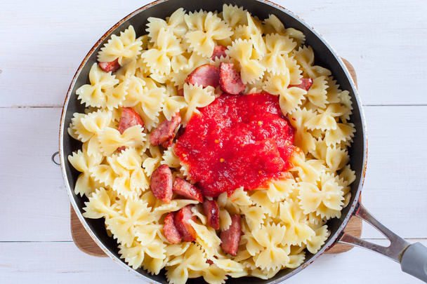 Step by step cooking pasta with sausage in tomato sauce with cheese, step 5 - adding tomato sauce, selective focus, top view - Fotó, kép