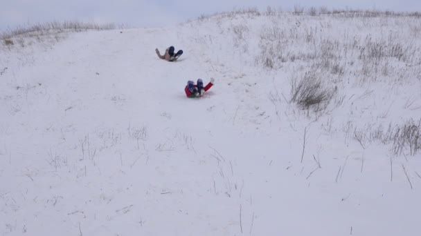 Happy kids gliding on sleds from high snowy mountain in winter park during Christmas holidays. Slow motion - Footage, Video