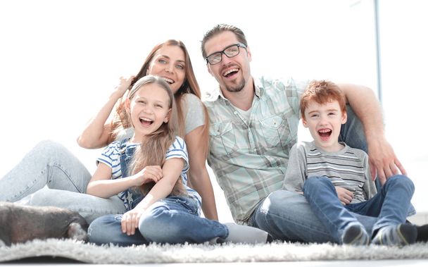 iloinen perhe istuu matolla uudessa olohuoneessa
 - Valokuva, kuva