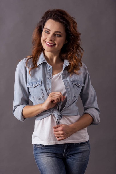 Portret van een jonge mooie vrouw op een grijze achtergrond glimlachen naar de camera - Foto, afbeelding