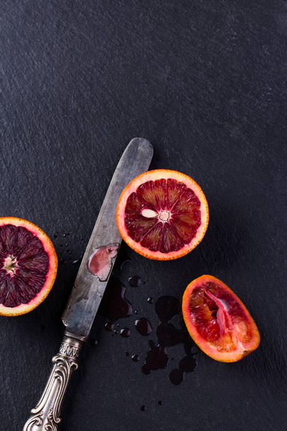 Whole and sliced sicilian oranges on a black slate background. - Photo, Image
