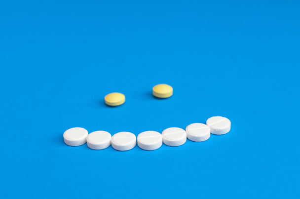 Smile of white and yellow pills on blue background. - Фото, зображення