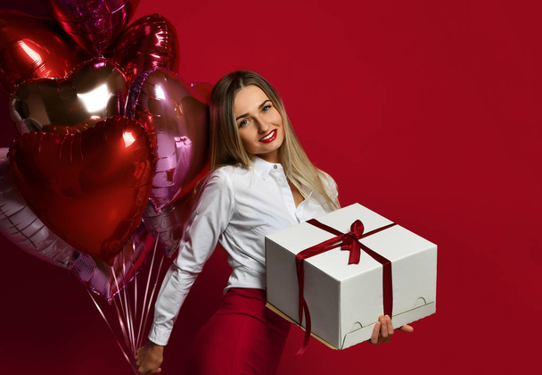Beautiful woman with present gift box and purple pink heart balloons happy smiling on red background - Fotografie, Obrázek