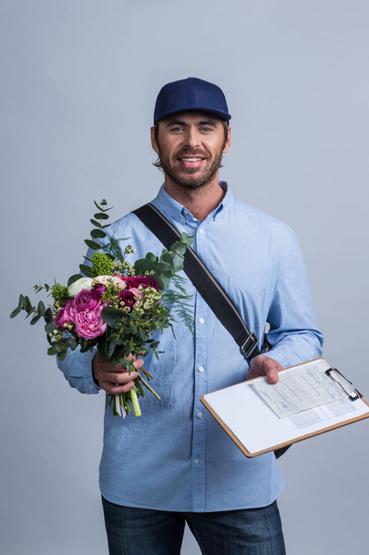 Delivery man holding flower bouquet and form - Zdjęcie, obraz