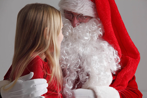 Little girl sitting on santa claus knees and talking to him - 写真・画像
