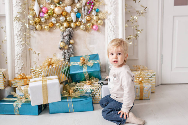 A little boy stands near a lot of gifts. Happy new year. decorated Christmas tree. Christmas morning in bright living room - Φωτογραφία, εικόνα