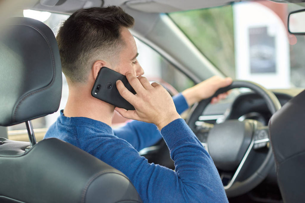 Young guy in sweater talking via cellphone while driving. - Photo, Image