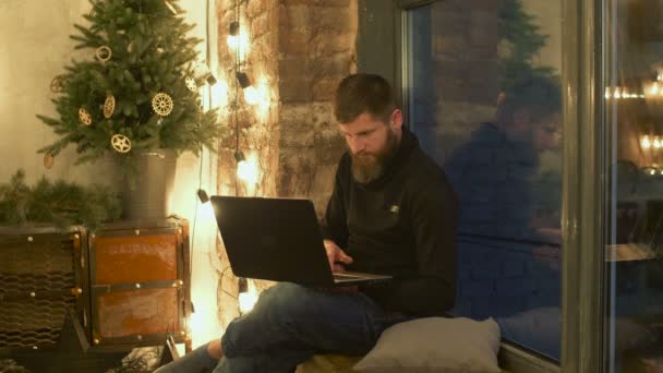 Male blogger with laptop sitting on windowsill - Záběry, video