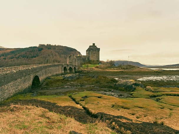 Marées dans le lac au château d'Eilean Donan, Écosse. Le pont pierreux populaire sur les vestiges de l'eau avec des touffes massives d'algues aquatiques. Faible lumière avec nuage bas
. - Photo, image