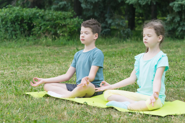 boy and girl are sitting in a lotus position on a green rug in the park - Foto, imagen