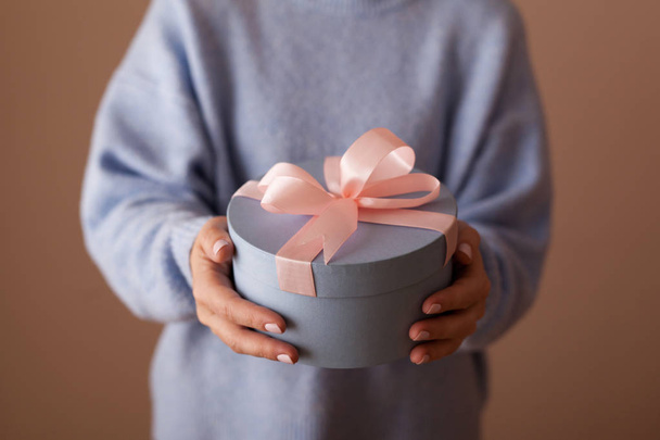 Beautiful round blue gift box with a pink bow in the hands of a woman - Фото, изображение