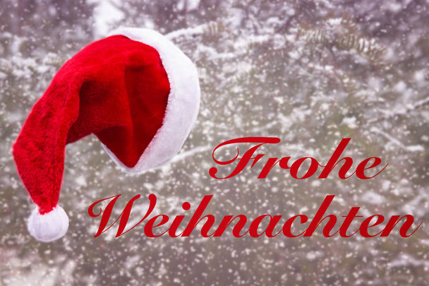 メリー クリスマスの雪とドイツ語で木からぶら下がっている赤いサンタ帽子 - 写真・画像