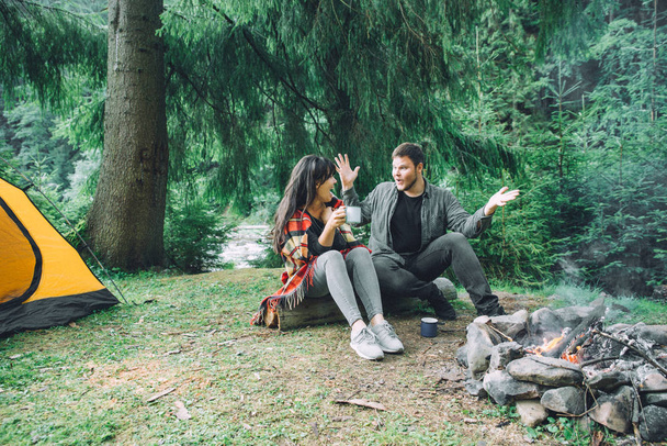 Pari istuu nuotion äärellä juomassa teetä ja kertomassa tarinoita. teltta ja suv taustalla. liitto luonnon kanssa
 - Valokuva, kuva
