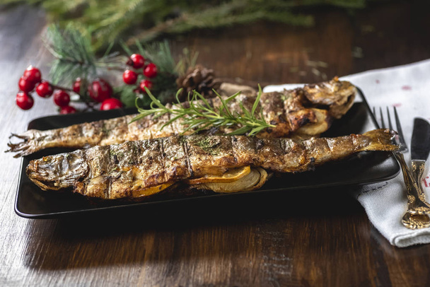 Grilled trout stuffed with vegetables on black plate - 写真・画像