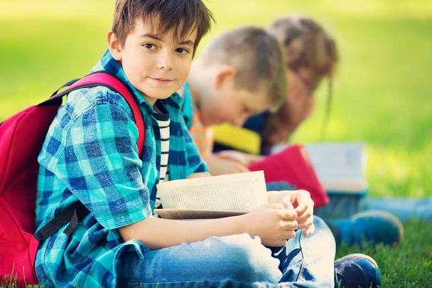 Children with rucksacks sitting in the park near school. Pupils with books and backpacks outdoors - Photo, Image