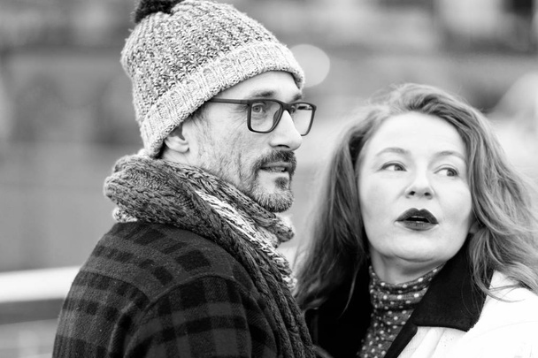 Portrait of expression couple talked on street. Couple looked off to strangers. Urban Couple speaks to smb on street. Brunette young woman and man in hat and glasses looks to afar. - Photo, image