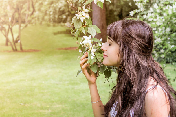 hübsches brünettes Mädchen mit langen Haaren, das eine Blume in der Natur riecht - Foto, Bild