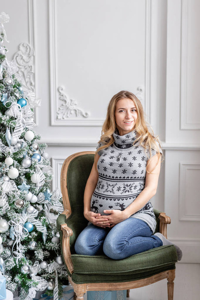 Portrait young pregnant mother. Happy new year. decorated Christmas tree. Christmas morning in bright living room. - Foto, afbeelding