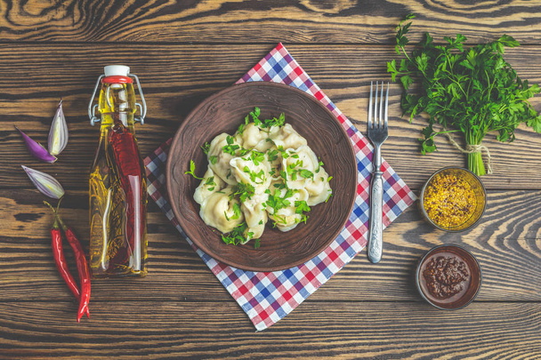 Tasty homemade meat dumplings or traditional italian ravioli of wholemeal flour sprinkled with fresh parsley on plate on dark wooden table surface, copy space, view from above. - Foto, Imagem