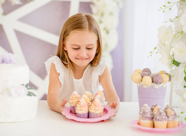 Little girl holding a pink plate with sweet cakes in the candy bar - Фото, изображение