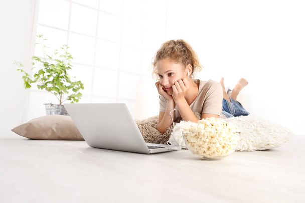 beautiful young woman watch a movie at the computer eating popcorn lying on living room wooden floor in comfortable home  - Photo, Image