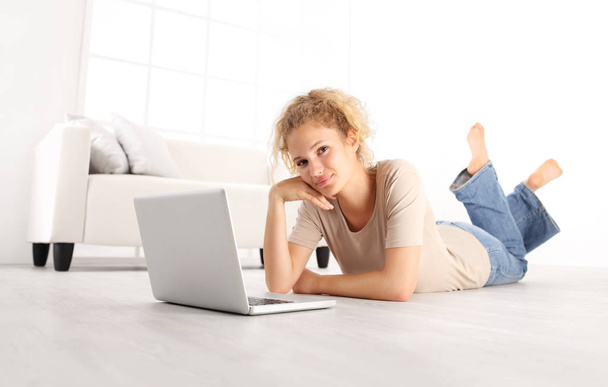sorrindo bela jovem com laptop de computador, deitado na sala de estar chão de madeira em casa branca confortável moderna
  - Foto, Imagem