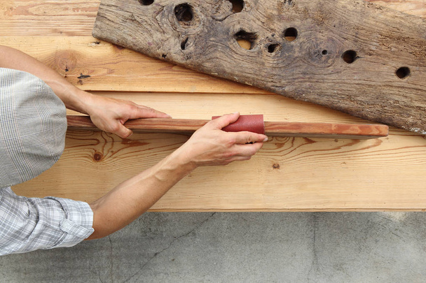 плотник, работающий на деревянной деревенской старой доске с песчаной бумагой, видом сверху и шаблоном копирования пространства
 - Фото, изображение